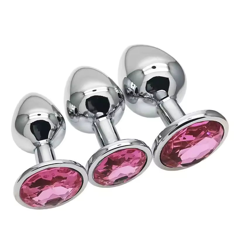 Three metallic butt plugs with pink gemstones on a white background